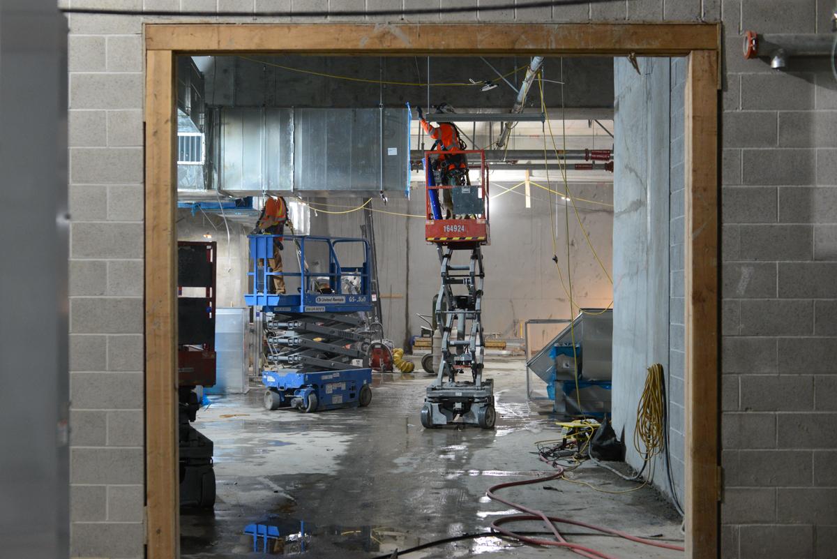Construction workers on elevated platforms installing rebar and ductwork inside a transit station headhouse under renovation.