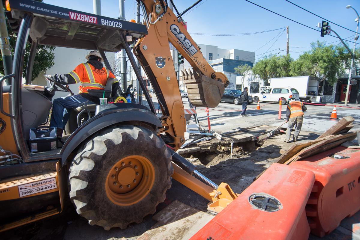 Construction worker operating excavator on 4th Street for Central Subway utility work in San Francisco.
