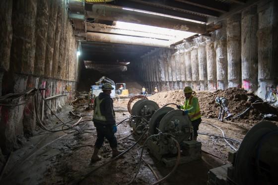 Workers in safety vests operate equipment inside an underground concrete tunnel during Central Subway construction.