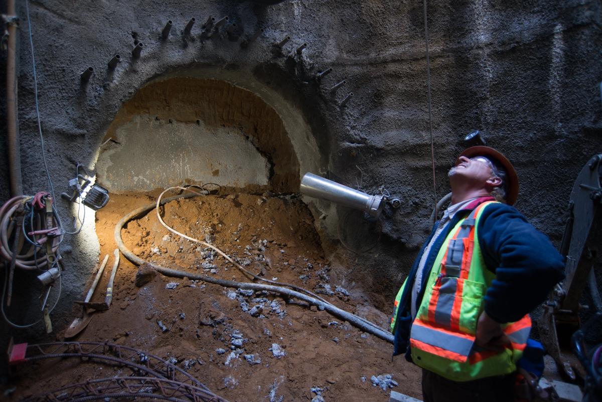 Worker in safety vest inspects large circular tunnel boring machine opening in underground construction site.
