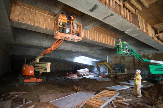 Workers on aerial lifts removing concrete forms beneath a transit station under construction