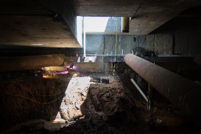 Underground excavation site with concrete walls, dirt, and natural light from above shaft opening.