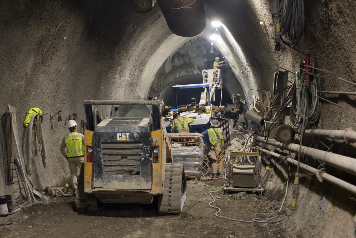Workers operate a CAT loader and drill rig inside a tunnel cavern during underground transit construction.