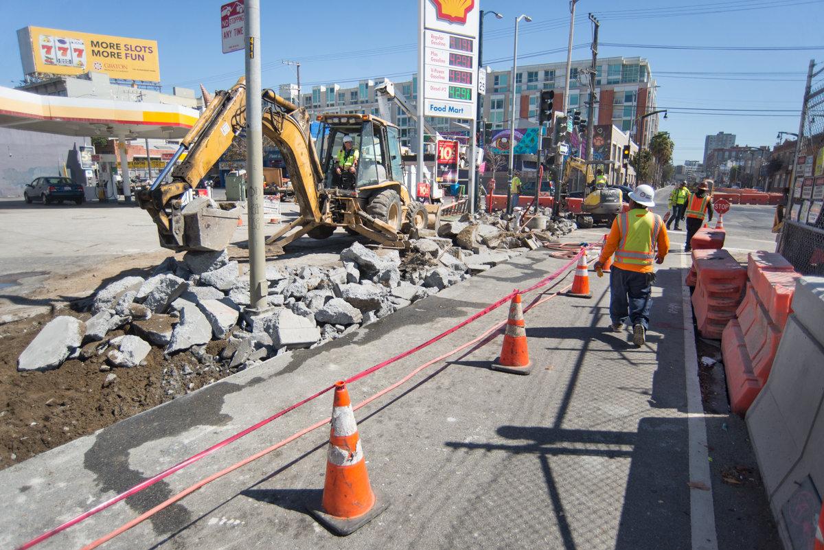 Construction crew operates excavator to remove concrete during Central Subway project sidewalk restoration on 4th Street.