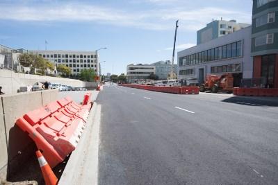 Red barrier fencing along 4th Street with construction equipment and vehicles visible on reopened roadway.