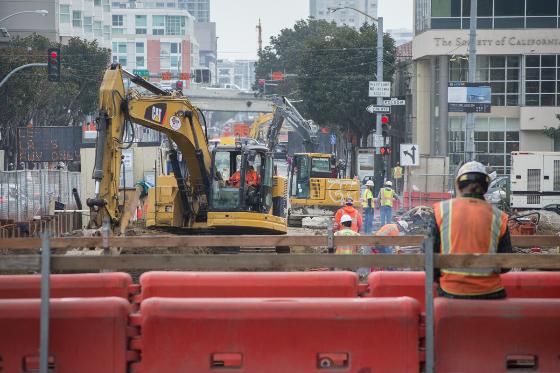 Construction workers operate yellow excavators on 4th Street during underground transit infrastructure work.