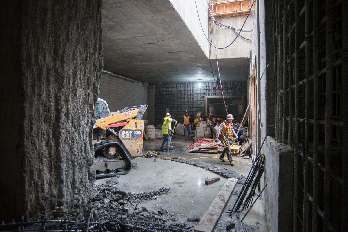 Construction workers in safety gear operate equipment inside an underground tunnel during ventilation structure preparation work.