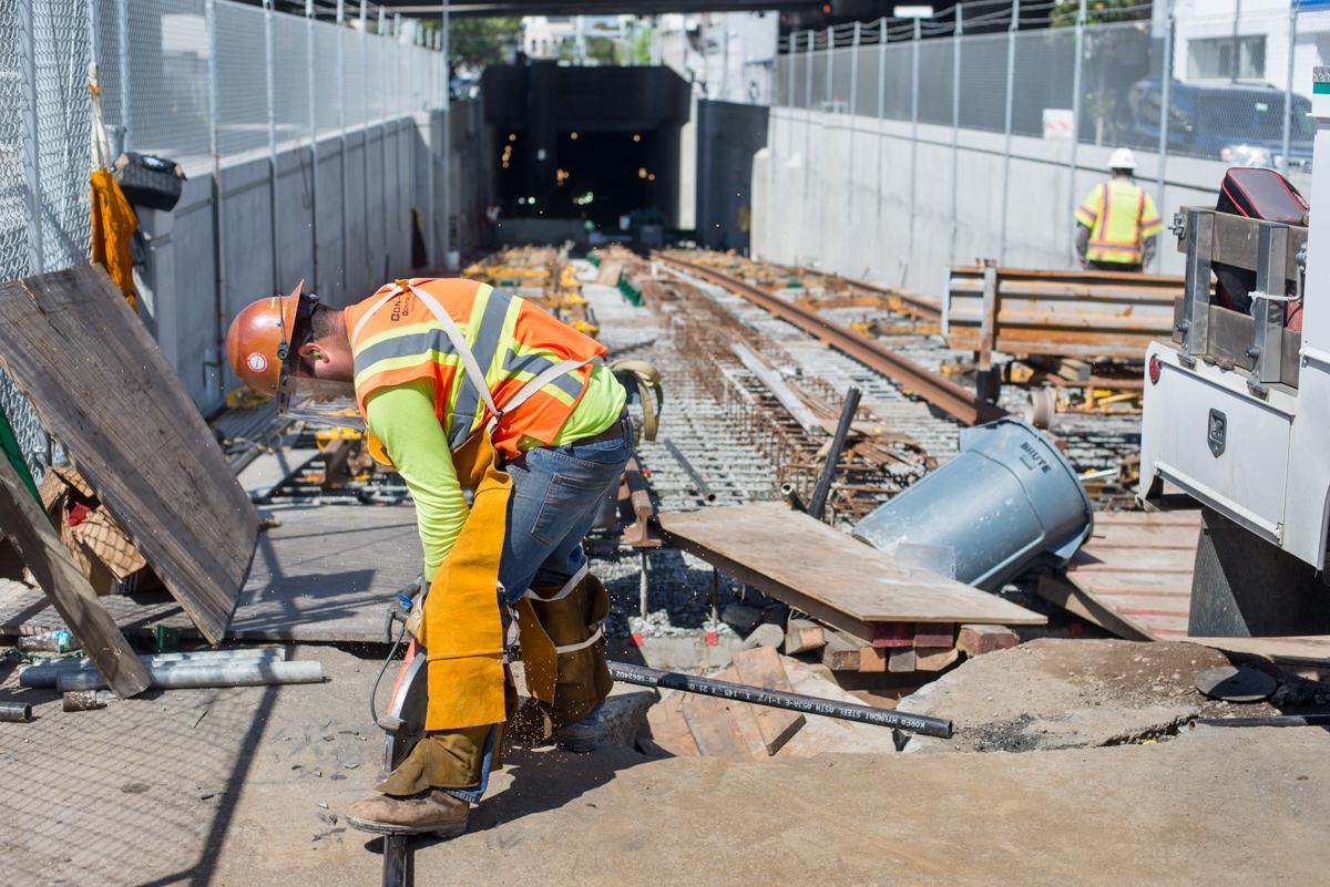 Worker in safety gear cutting pipe at tunnel portal construction site on 4th Street