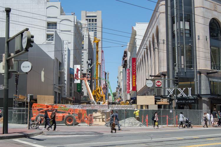 Construction equipment and barriers on Stockton Street with lane closures and flaggers managing traffic flow.