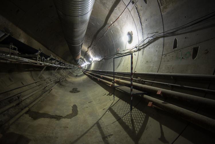 Interior of subway tunnel under construction with tunnel boring machine and metal pipes along the walls.