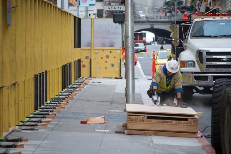 Worker in safety gear installing yellow decorative barricade on Stockton Street construction site with truck nearby.