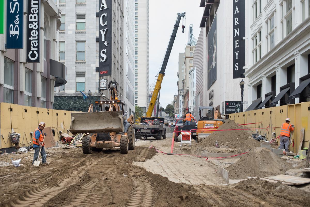 Construction site at Union Square/Market Street Station with heavy equipment, workers, and yellow safety barriers along downtown street.