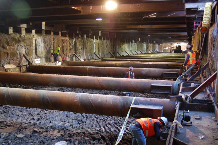 Workers in safety vests installing large pipes and rebar in an underground transit tunnel construction site.