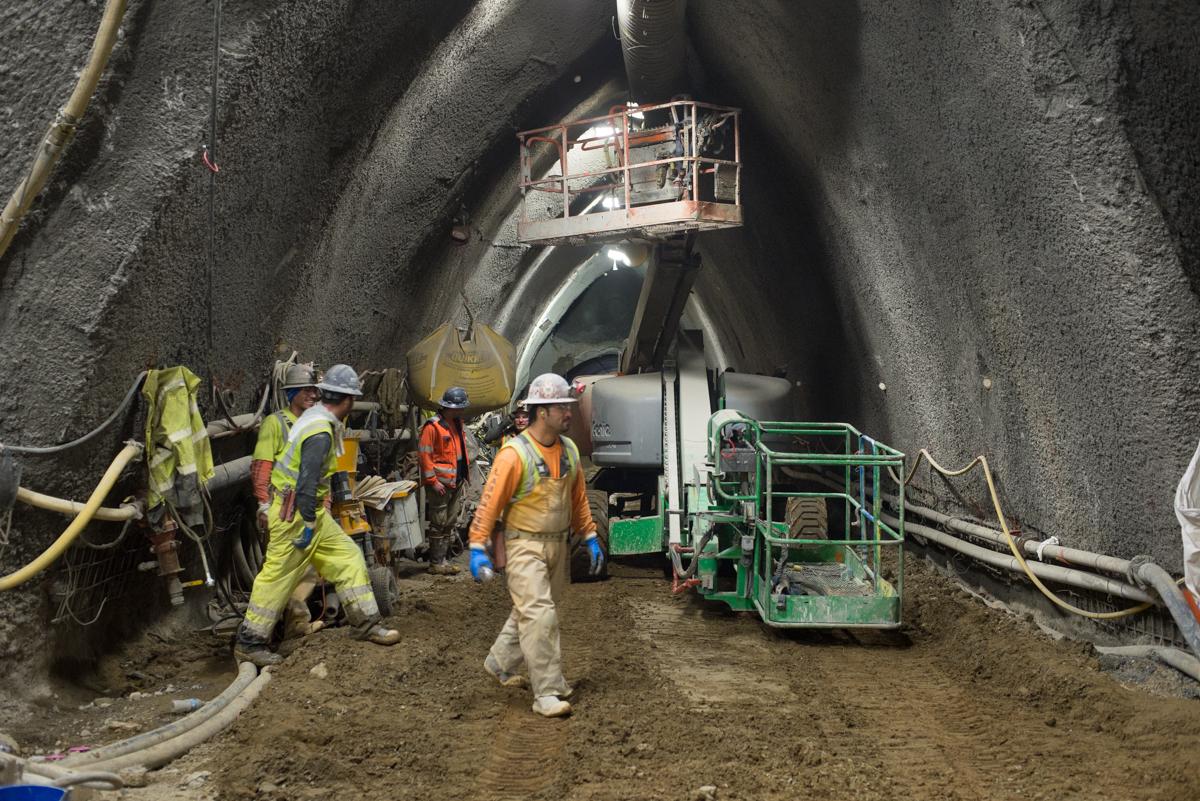 Workers in safety gear operate equipment inside an underground tunnel cavern during construction excavation work.