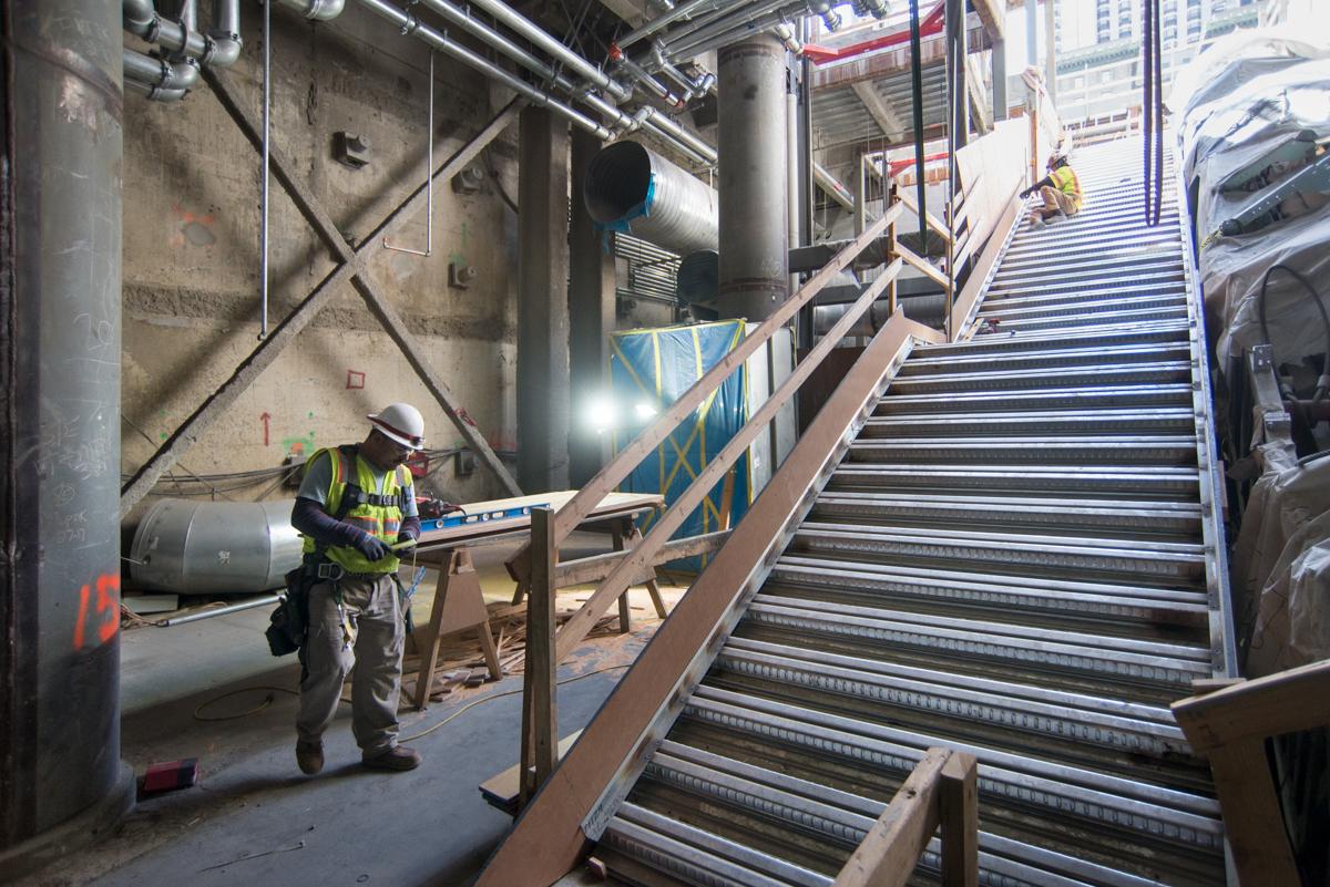 Construction worker in safety gear installing temporary railing on interior staircase at Union Square station.