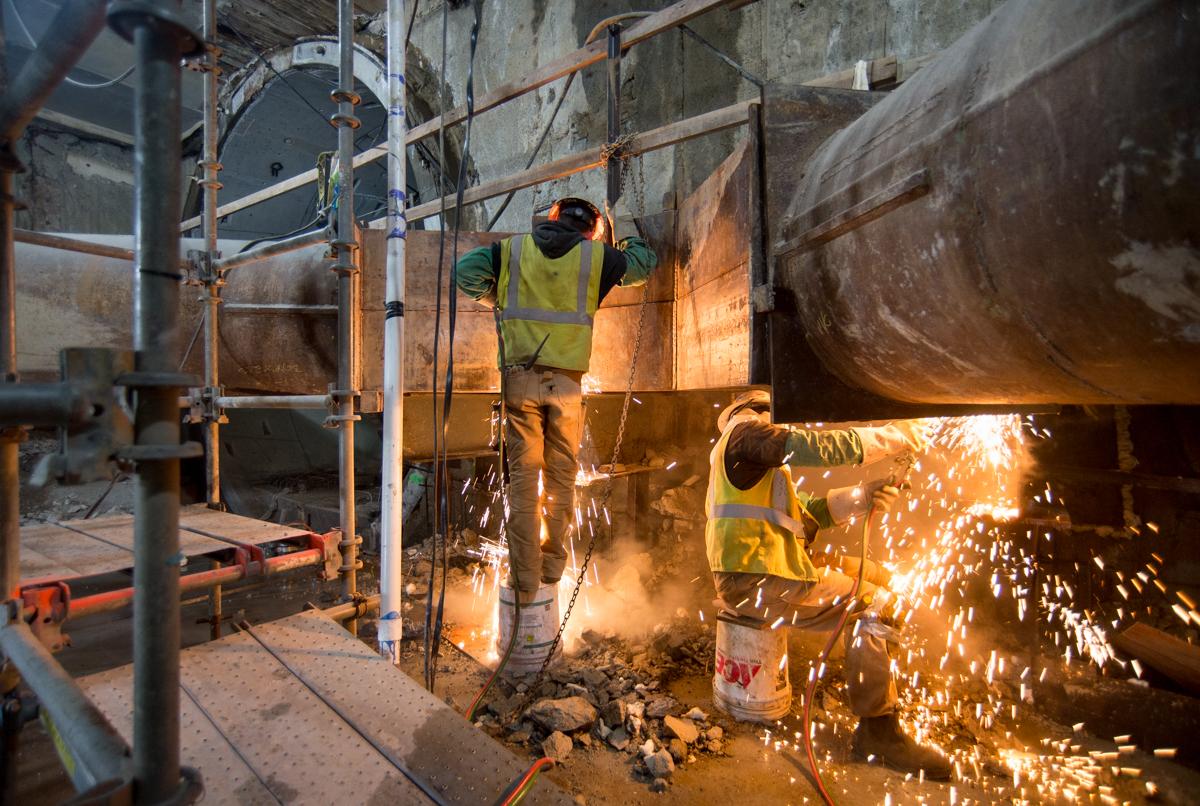 Workers in safety vests welding metal infrastructure during Central Subway construction.
