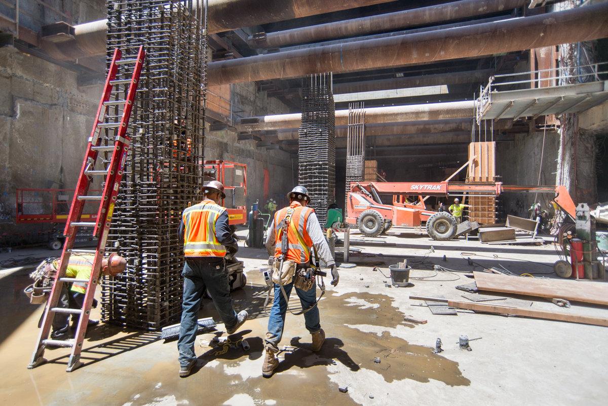 Construction workers installing rebar cages for columns inside transit station headhouse.