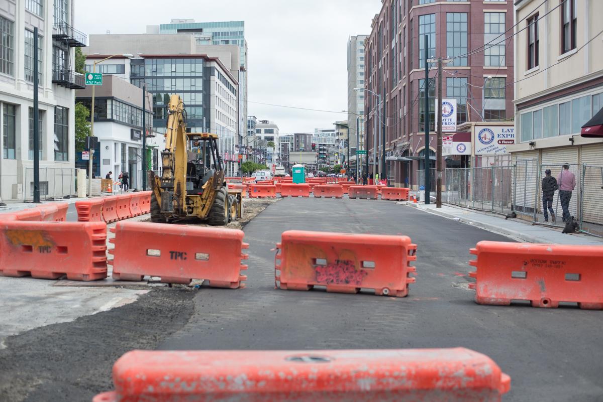 Construction site on 4th Street with orange barriers, excavator, and urban buildings in background.