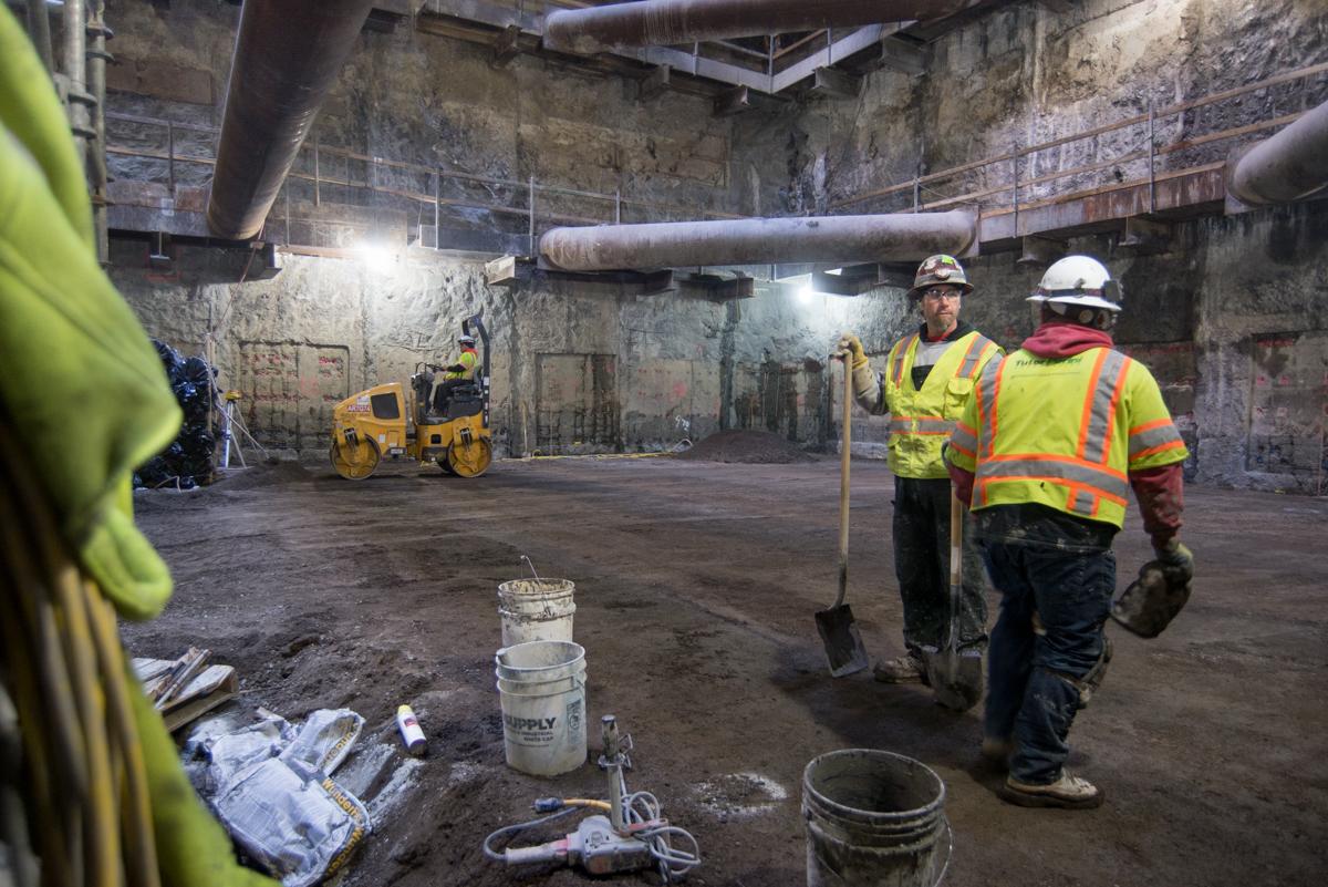 Construction workers in safety vests excavate underground transit tunnel with equipment and machinery visible.