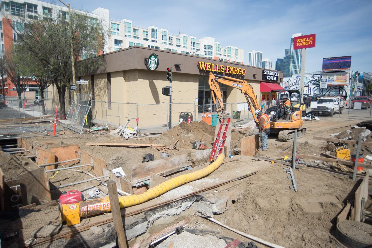 Construction site on 4th Street with backhoe backfilling utility trench near Wells Fargo storefront.
