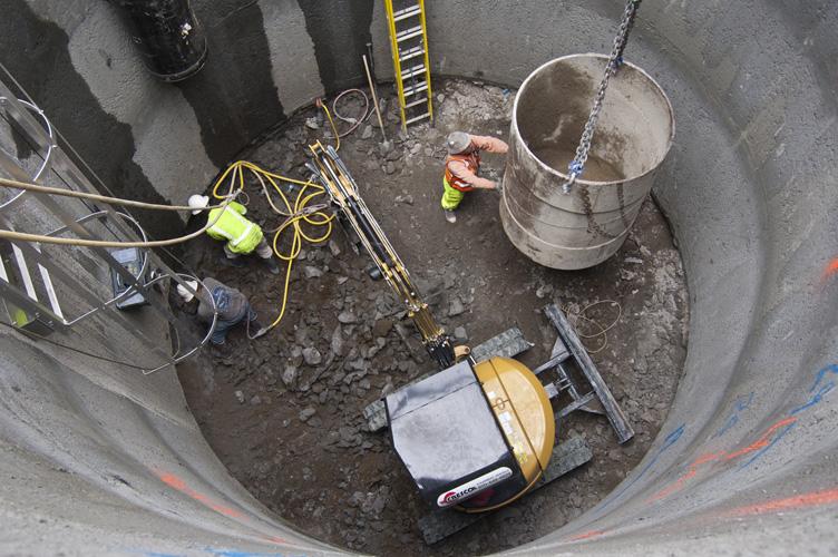 Workers in safety gear performing underground construction work in a concrete shaft with equipment and materials.