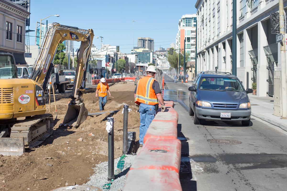 Construction crew working on underground utility installation on city street with excavator and traffic control.