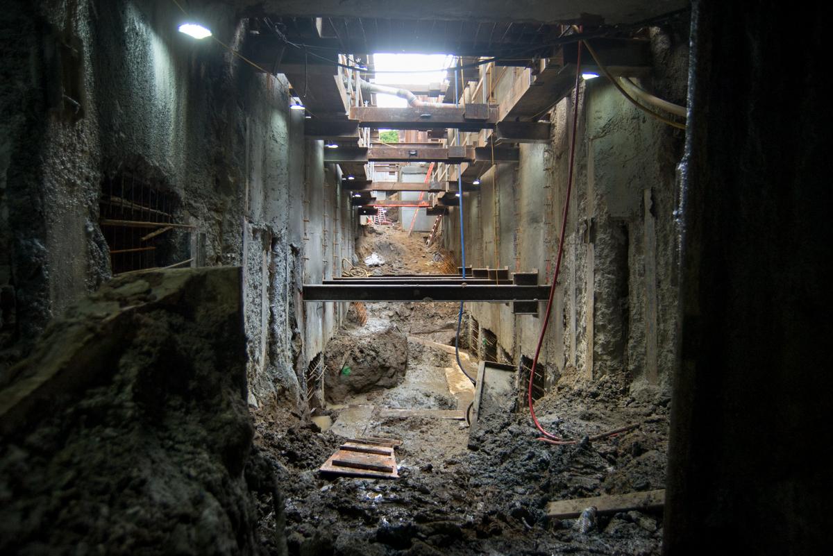 Underground tunnel with concrete walls, steel bracing, and construction equipment visible under street level.