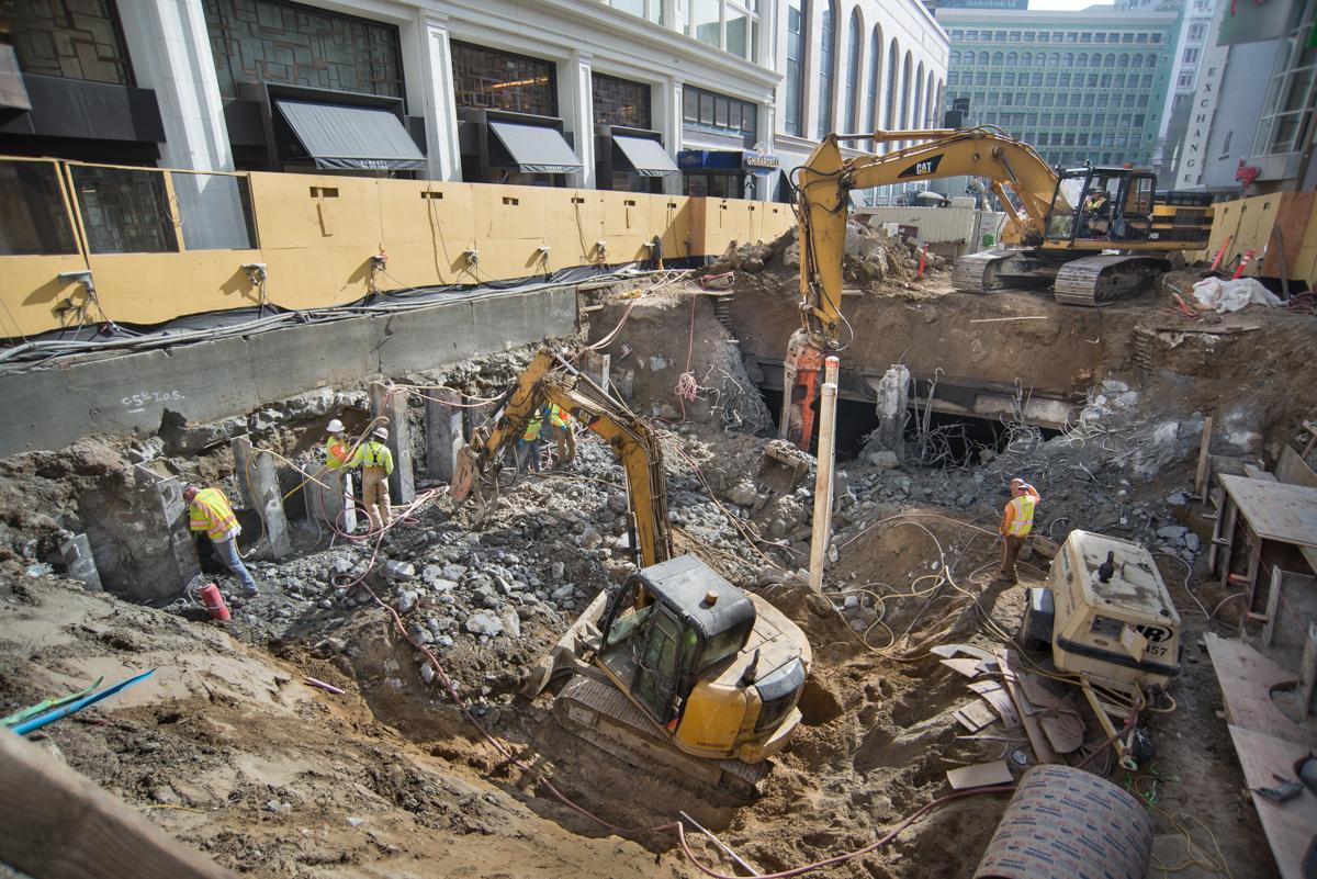 Construction site on Stockton Street with excavators, workers in safety gear, and deep trenches for underground work.