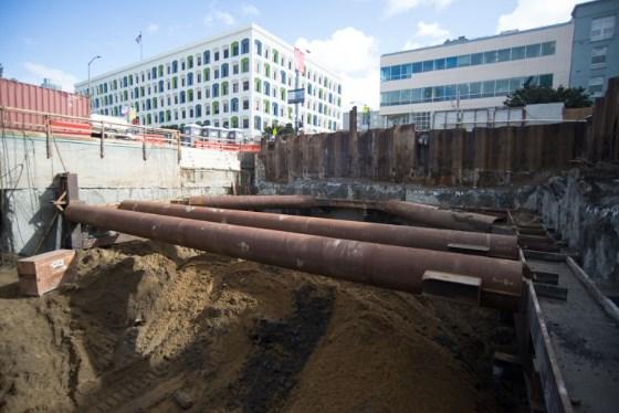 Steel walers spanning excavated station box at Yerba Buena-Moscone Street construction site with downtown buildings visible.