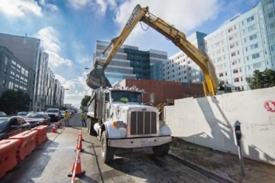 Excavator with extended arm loading soil into dump truck at urban construction site