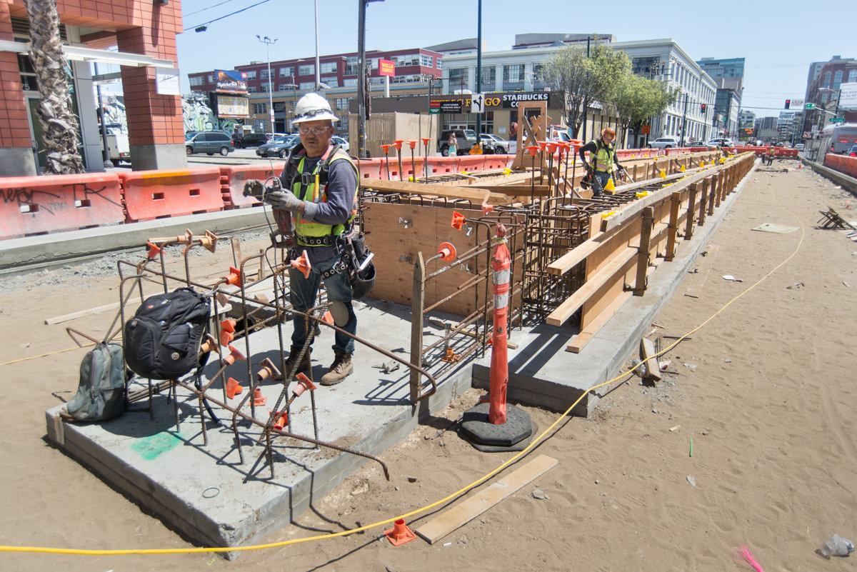 Worker in hard hat and safety gear inspecting equipment at subway tunnel construction site with red barriers and wooden forms.