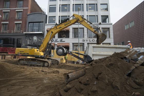 Yellow excavator loads soil into dump truck at Stockton and Geary construction site.