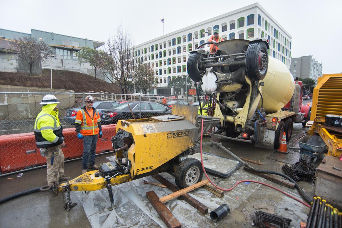 Construction workers operate concrete mixer truck and equipment at underground station excavation site.