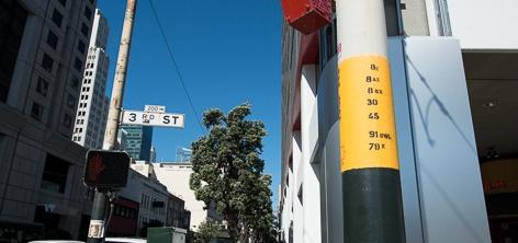 Yellow and black bus stop pole on urban street with buildings and clear sky visible.