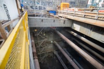 Construction site showing excavated pit with large pipes and steel reinforcement structures during transit station headhouse construction.