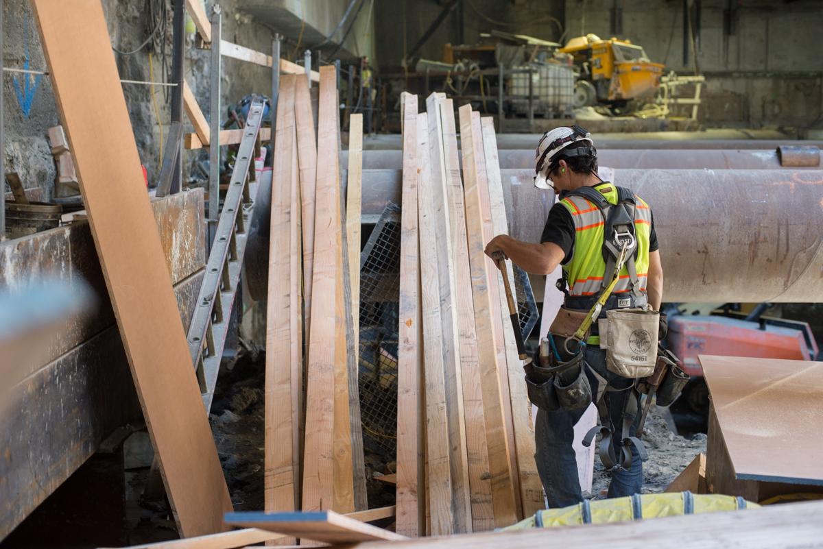 Worker in safety gear assembling concrete forms inside underground transit station construction site.