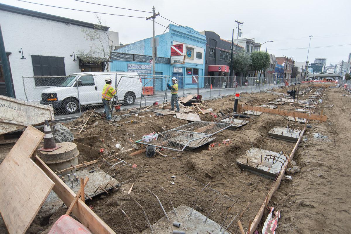 Construction workers install safety fencing at 4th and Brannan surface station work area for Central Subway Project.