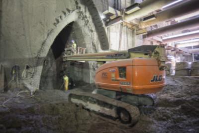 Orange tracked excavator inside underground cavern with concrete walls and overhead lighting.