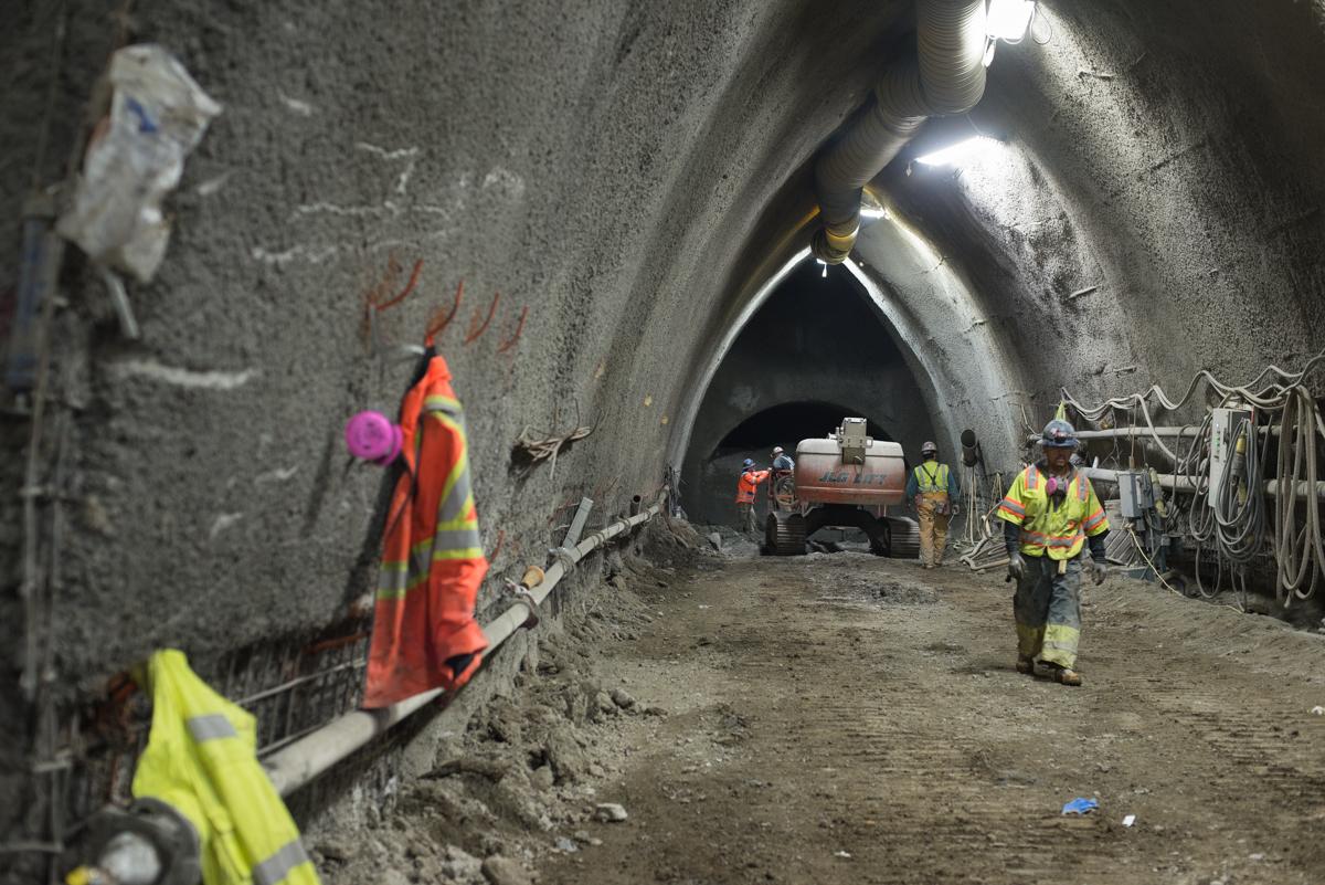 Workers in safety vests inside tunnel excavation site with equipment and lighting