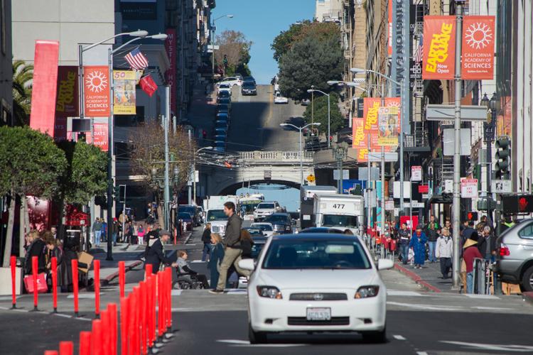 Stockton Street pedestrian and vehicle traffic with red bollards, storefronts, and city buildings.