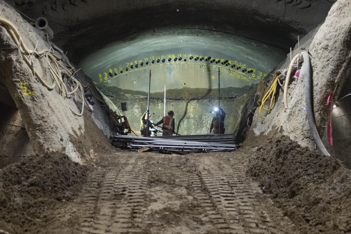Workers on platform inside tunnel excavation with yellow safety markings and equipment.