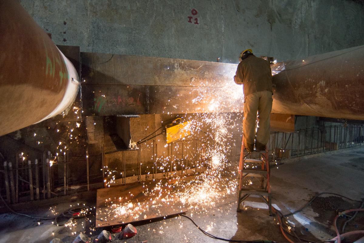 Worker cutting steel beam with sparks during station platform construction.