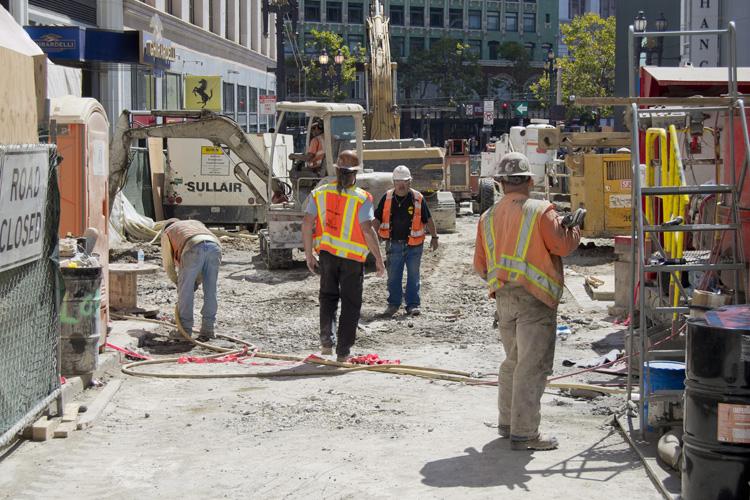 Construction workers and equipment on Stockton Street during roadway restoration project in downtown area.