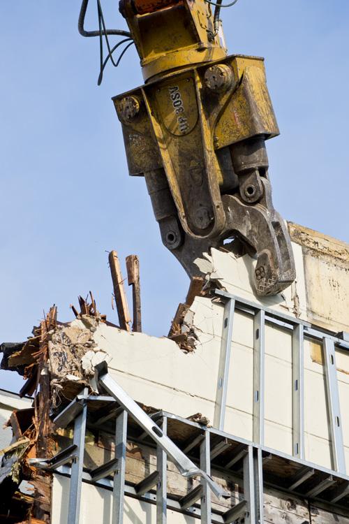 Heavy demolition equipment with hydraulic jaw removes concrete debris from Pagoda Palace building facade.