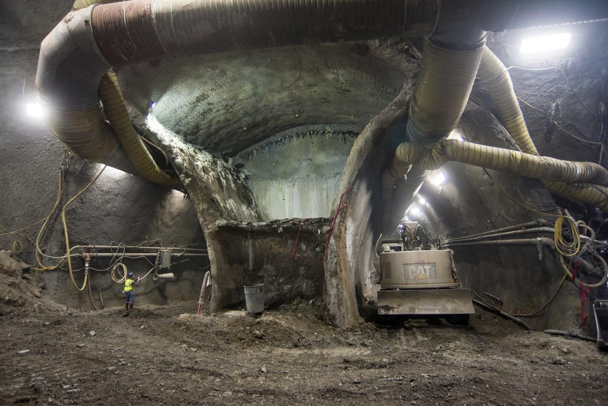 Underground tunnel construction site with excavated concrete header, support pipes, and worker in safety gear.