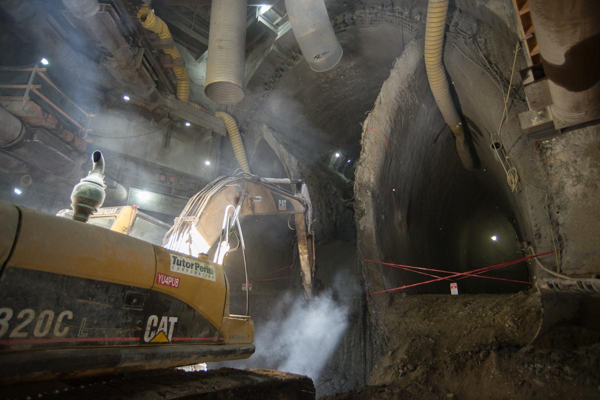 Bulldozer collecting excavated material inside underground tunnel construction site with dust and work lights.