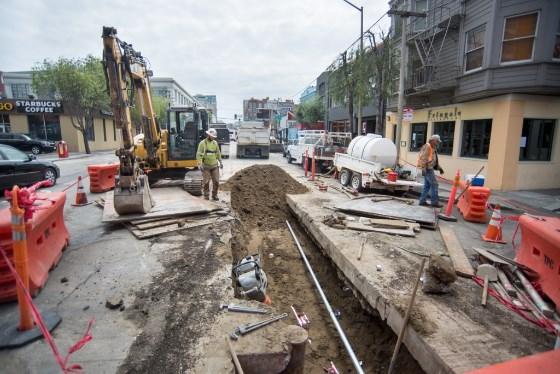 Construction crew operates excavator while backfilling trench on 4th Street for subway project.