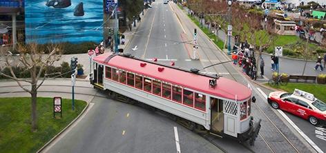 Red and white vintage streetcar traveling on Market Street with pedestrians and buildings visible alongside the track.