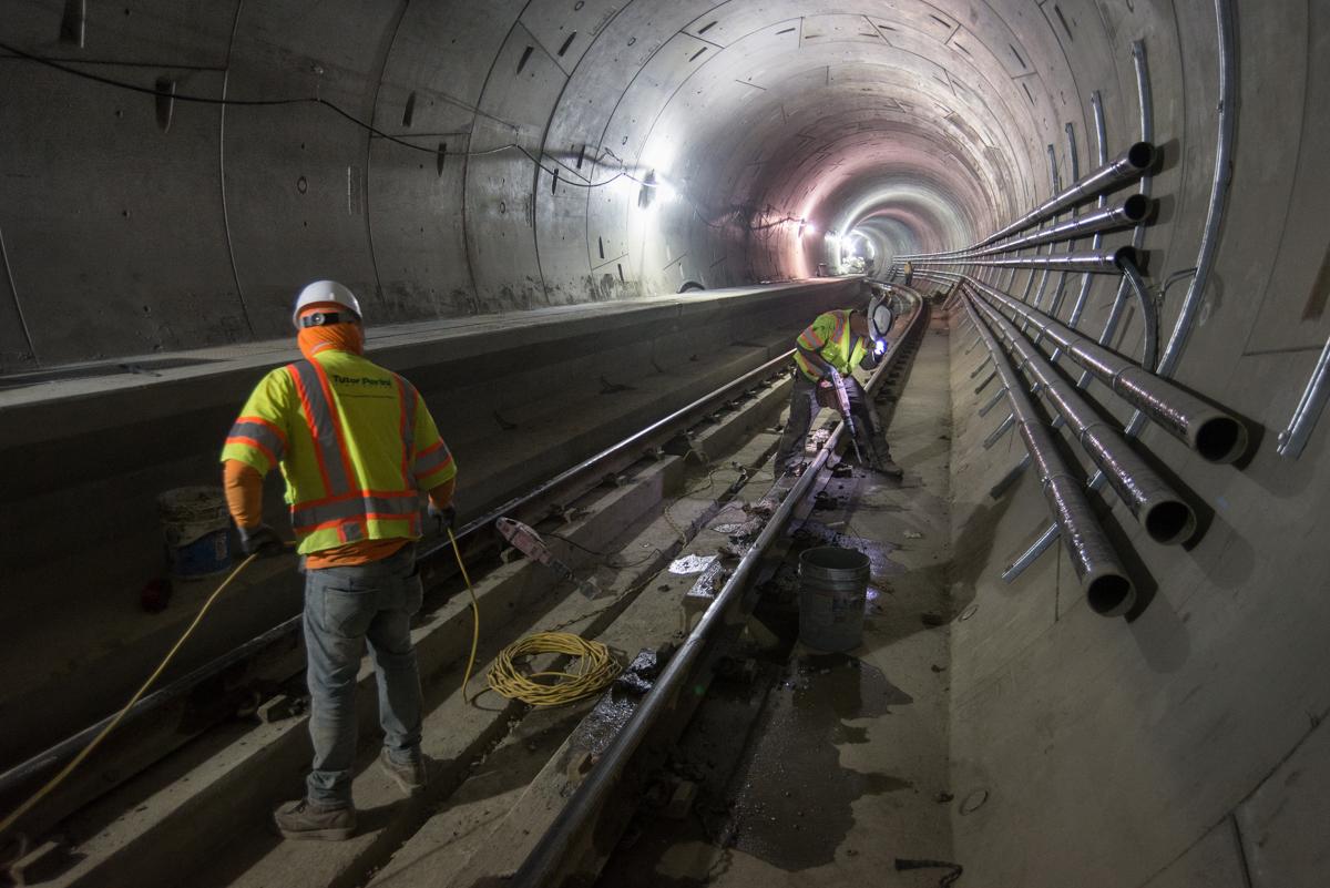 Worker in safety gear inspecting railroad tracks in underground tunnel at Chinatown Station.