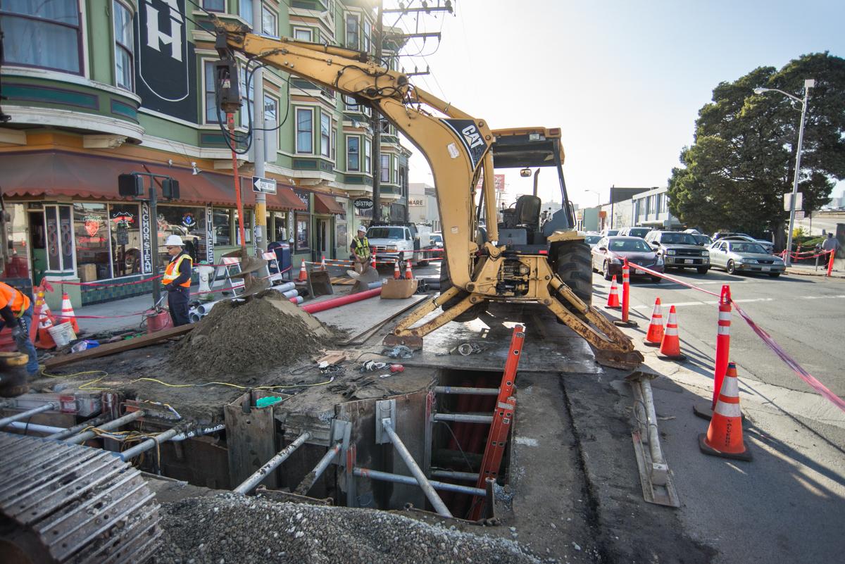 Backhoe excavating utility trenches at 4th and Bryant Street for Central Subway construction.